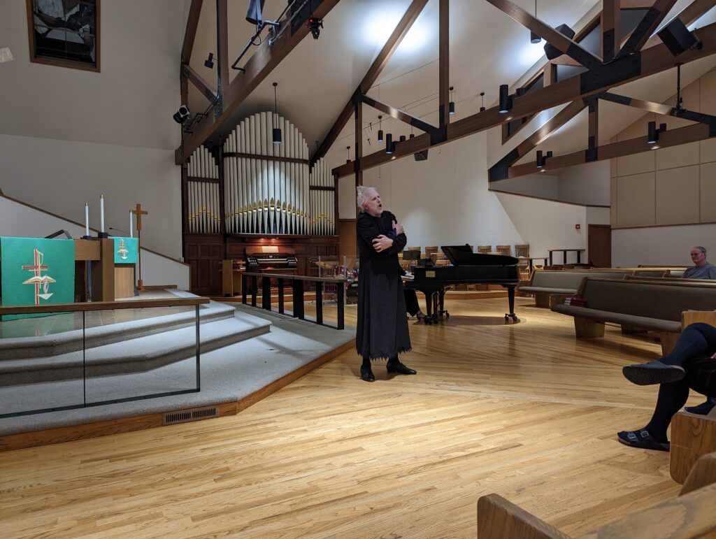 Man singing in long black robe with organ and piano in background