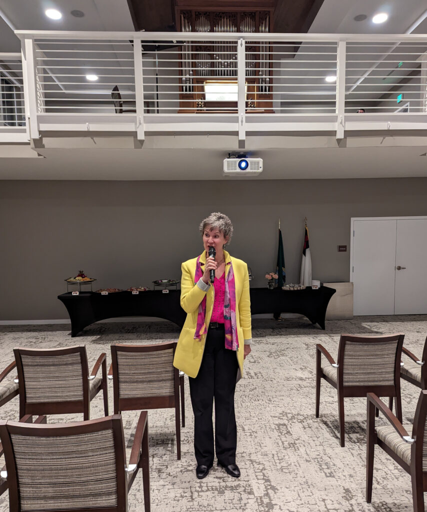 Woman in yellow jacket standing in the front of a room holding a microphone