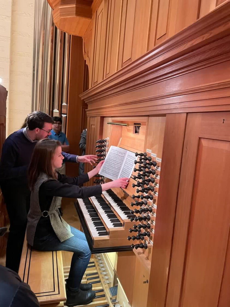 Girl sitting at organ bench surrounded by several people