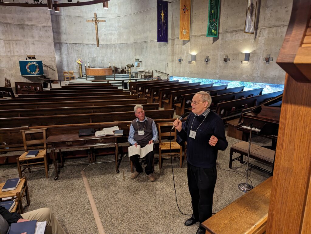 man with microphone stands beside organ bench