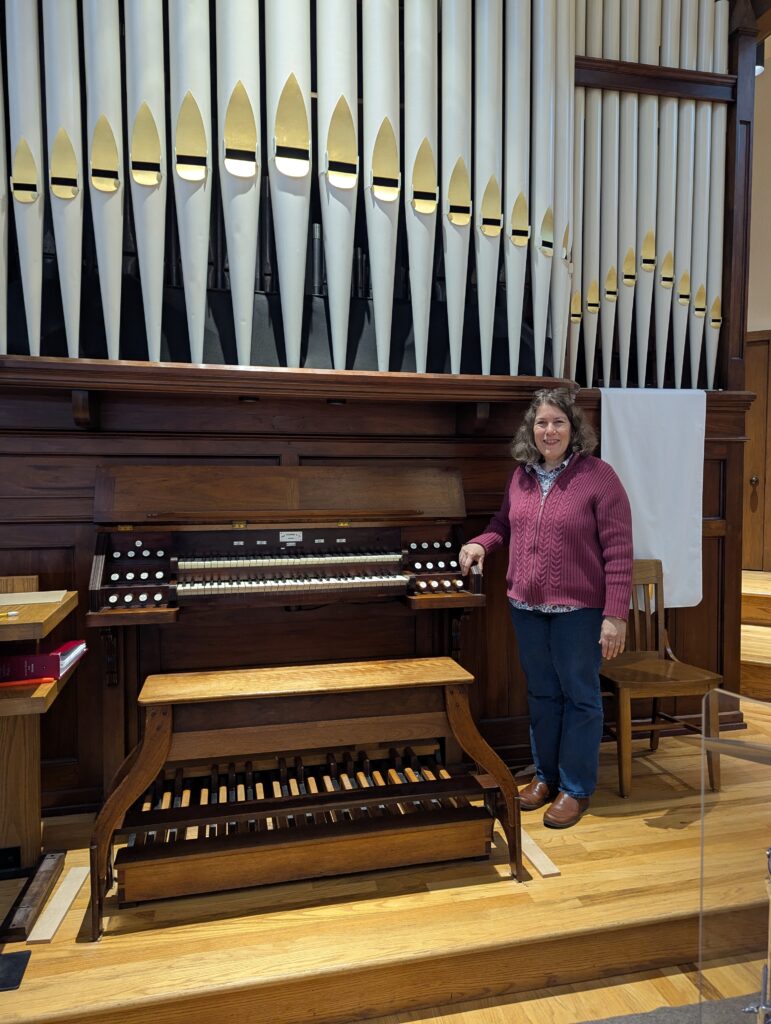 A woman stands in front of an organ in a church