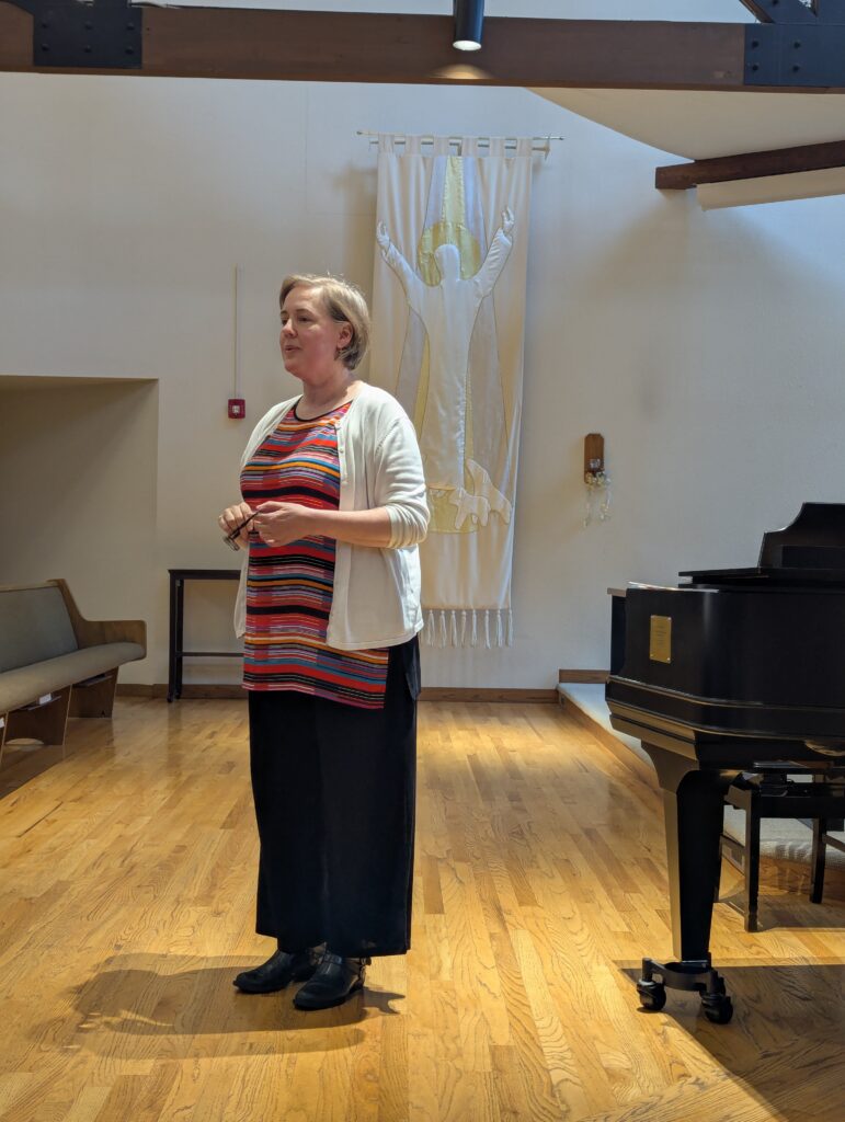 A woman in a thoughtful pose stands beside a piano in a church